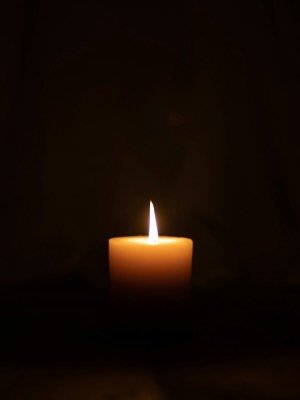 An amber candle flame and stick radiates from a black background.